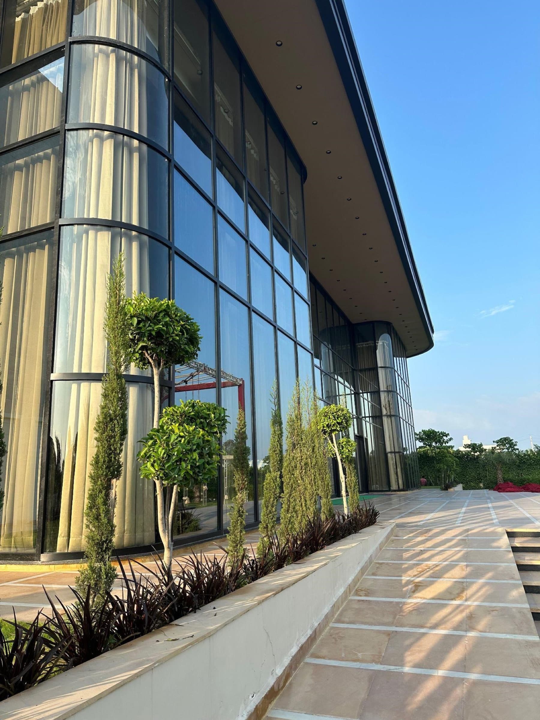 Glass curtain-wall facade of The Emerald above a paved forecourt with topiary planting