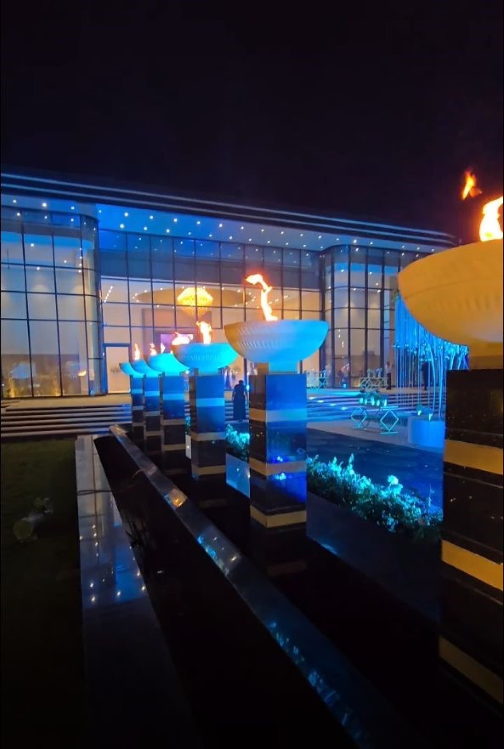 Night view of the forecourt with an illuminated water channel and flame bowls